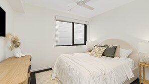 Un dormitorio con cama, mesita de noche, lámpara y ventana.