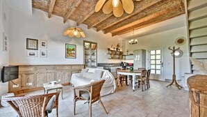 Un espacio habitable amplio con un sofá grande, sillas de mimbre, una mesa de comedor y una cocina al fondo.