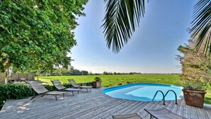 Una terraza de madera con piscina, sillas de descanso y vistas a un campo verde.