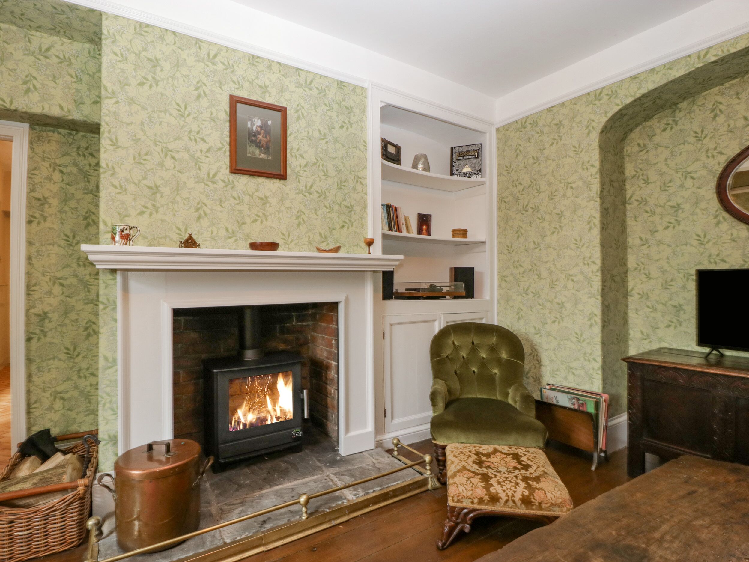 A cozy living room with a fireplace, a green armchair, and a bookshelf.