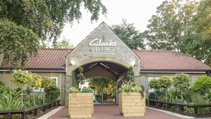 La entrada a Clarks Village, con un arco de piedra, sendero de ladrillo y macetas de madera con follaje.