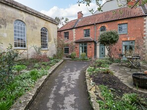A courtyard with a narrow pathway flanked by brick buildings, one with a large arched window and the other with multiple windows and a door. - Kylemore (Glastonbury)