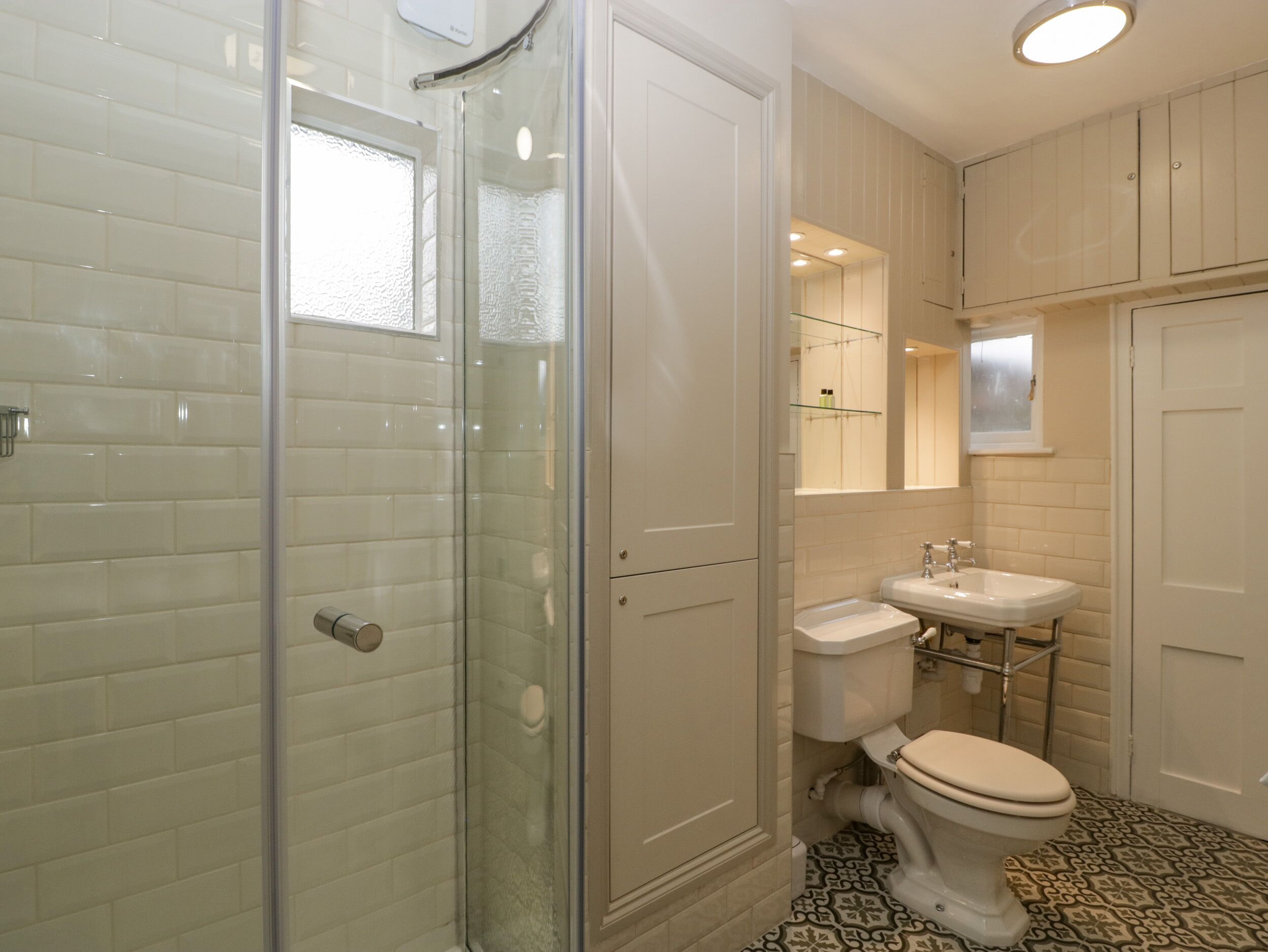 A bathroom with a glass shower enclosure, a toilet, a sink, and a mirror.