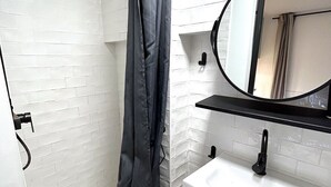 A bathroom with a shower, a sink, a mirror, and a patterned floor. - Loft Varenne (Paris)