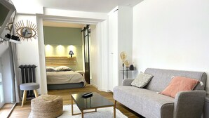 A modern living room with a grey sofa, a small round ottoman, a glass coffee table, and a white rug. - Loft Varenne (Paris)