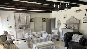 Un salon chaleureux avec un canapé, un fauteuil et un pouf, une armoire blanche et une cheminée.