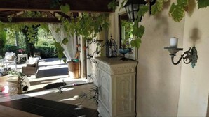 Un patio couvert comprenant un banc en pierre, des plantes en pot et un mur décoratif agrémenté d’une étagère et d’une lampe fixée au mur.