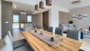 A modern living room with a wooden dining table, grey upholstered chairs, a grey sofa, and a staircase leading to an upper level.