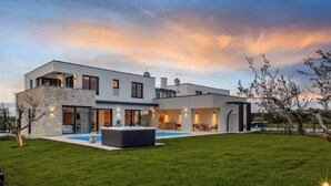 A modern two-story house with a swimming pool, outdoor seating area, and a stone facade.