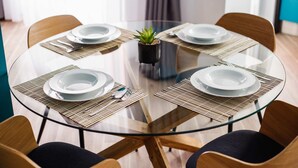 A round glass table with four chairs, each with a placemat. A small potted plant is centered on the table. - Azur Paradise near City Center (Oradea)