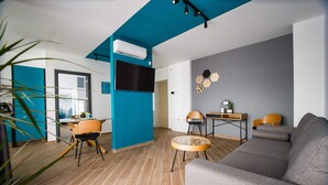 A modern living room with a grey sofa, wooden flooring, a blue accent wall, and a flat-screen TV mounted on the wall. - Azur Paradise near City Center (Oradea)
