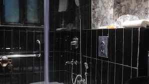 A bathroom with a glass-enclosed shower, a white toilet, and a black sink. - The Saga Hotel (New Delhi)