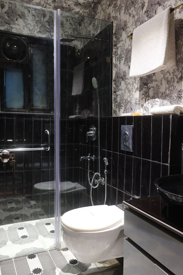 Une salle de bain avec une douche à parois de verre, des toilettes blanches et un lavabo noir.