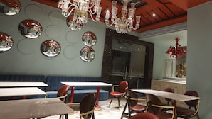 A restaurant interior with round mirrors on the wall, a chandelier, and red upholstered seating. - The Saga Hotel (New Delhi)