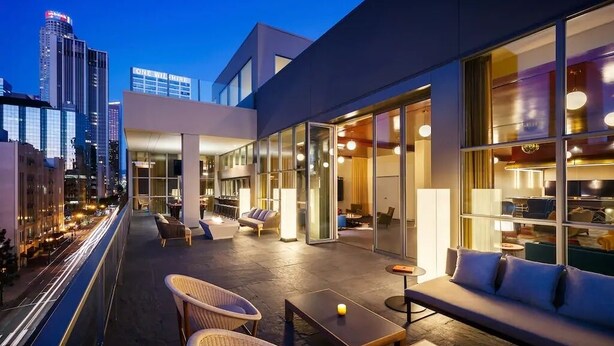 A rooftop lounge with seating and tables, large windows, and a city view. - 1B1B  DTLA (Los Angeles)