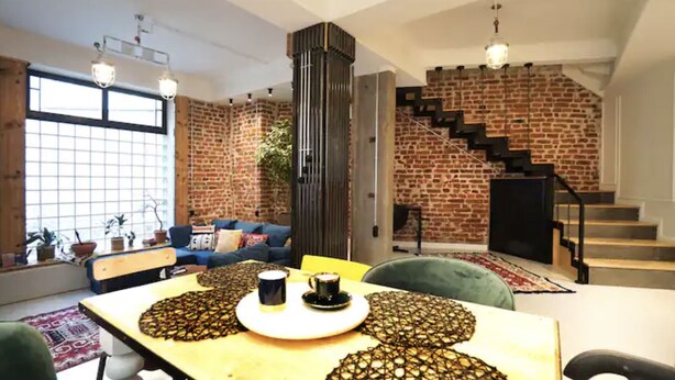 Una sala moderna con pared de ladrillo, una escalera y un comedor con mesa dispuesta para dos.
