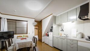 A compact kitchen with a dining area, featuring a TV, a dining table with chairs, and a small refrigerator. - 10mins train to Namba, 4mins walk to stn, 2floor Japanese style whole house (大阪市)