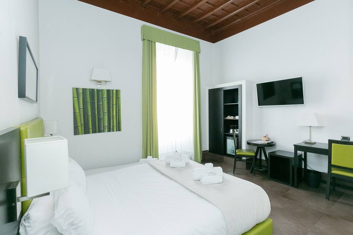 A hotel room with a bed, a desk, a chair, a TV, and a wardrobe.