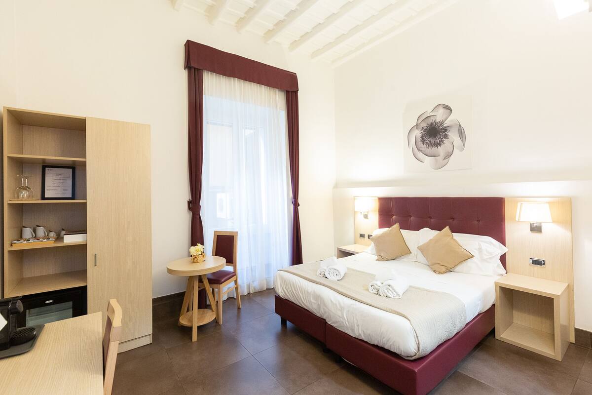 A hotel room with a large bed, a desk, a chair, and a small table.