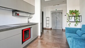 Eine moderne Küche mit Einbauofen, grauer Arbeitsplatte und roter Ofentür. Im Wohnbereich befindet sich ein blaues Sofa und eine Pflanze.