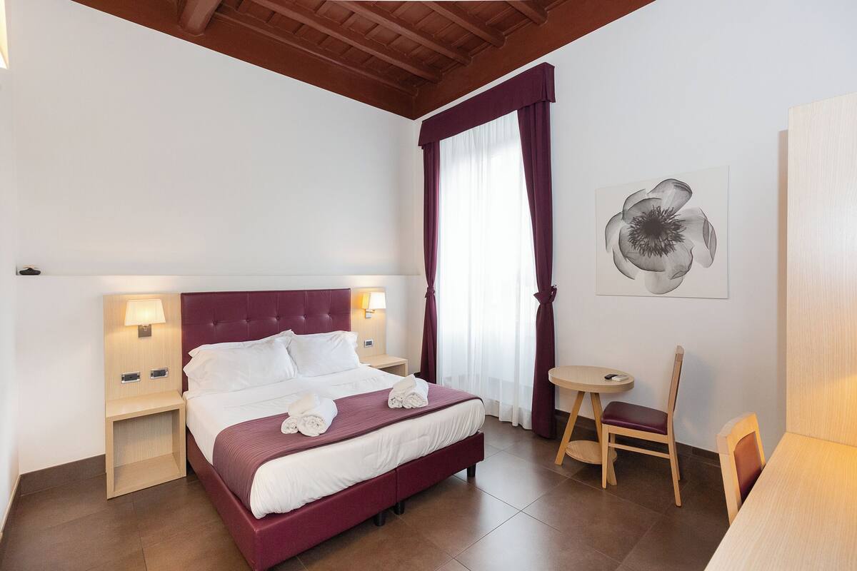 A hotel room with a large bed, two bedside tables with lamps, a small round table, and a chair.