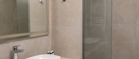 A modern bathroom with a large white sink, a glass shower enclosure, and a mirror above the sink.
