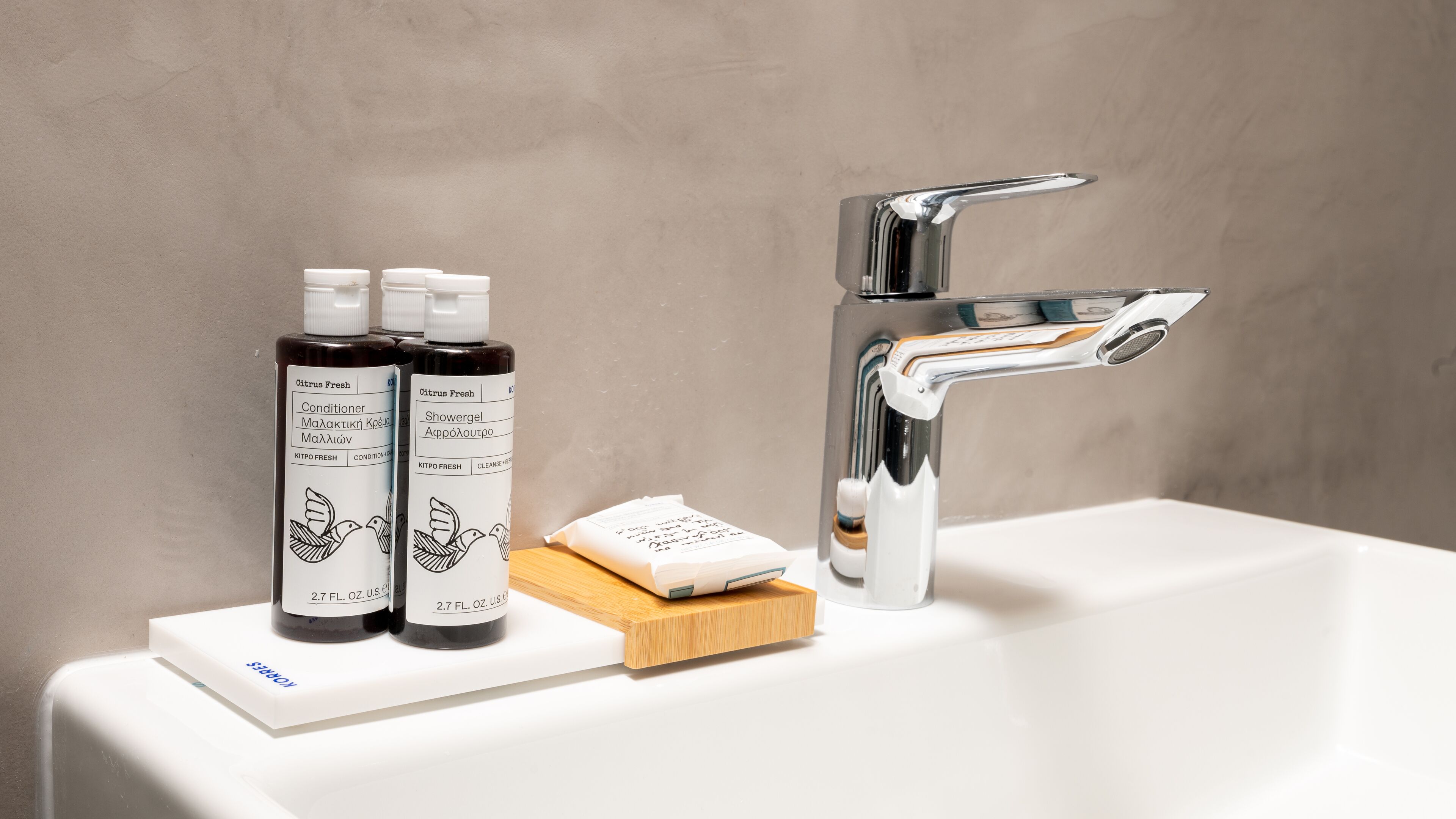 A bathroom sink with two bottles of Citrus Fresh products, a handheld showerhead, and a wooden soap dish.