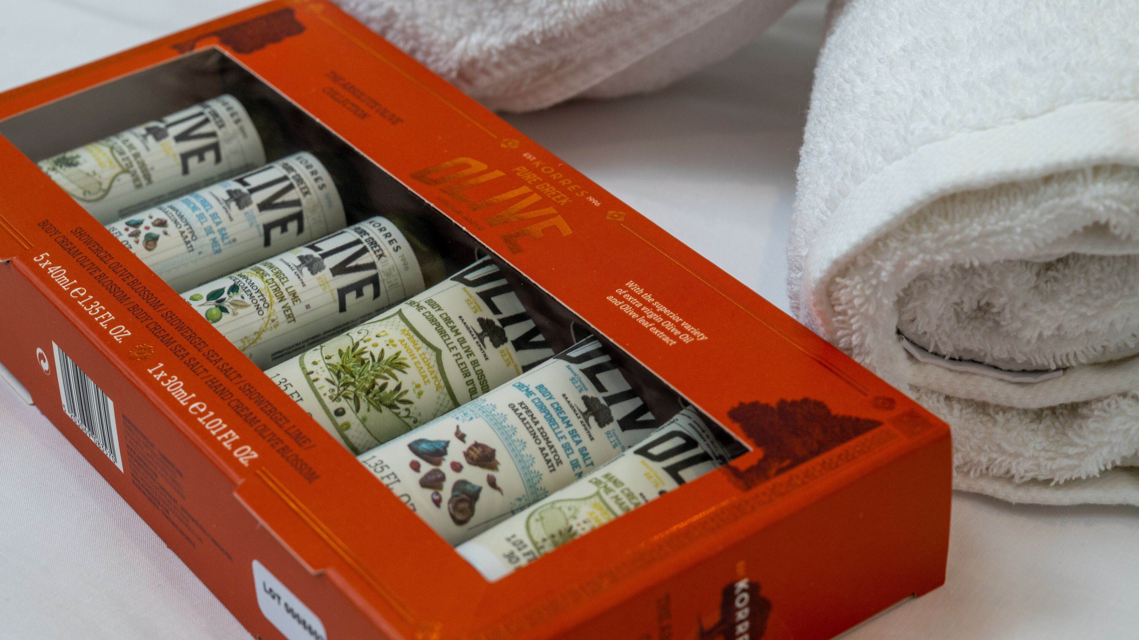 A box of body care products with visible labels and a rolled white towel in the background.