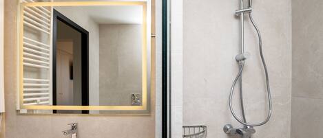 A modern bathroom with a large mirror, a sink, and a shower with a handheld showerhead.