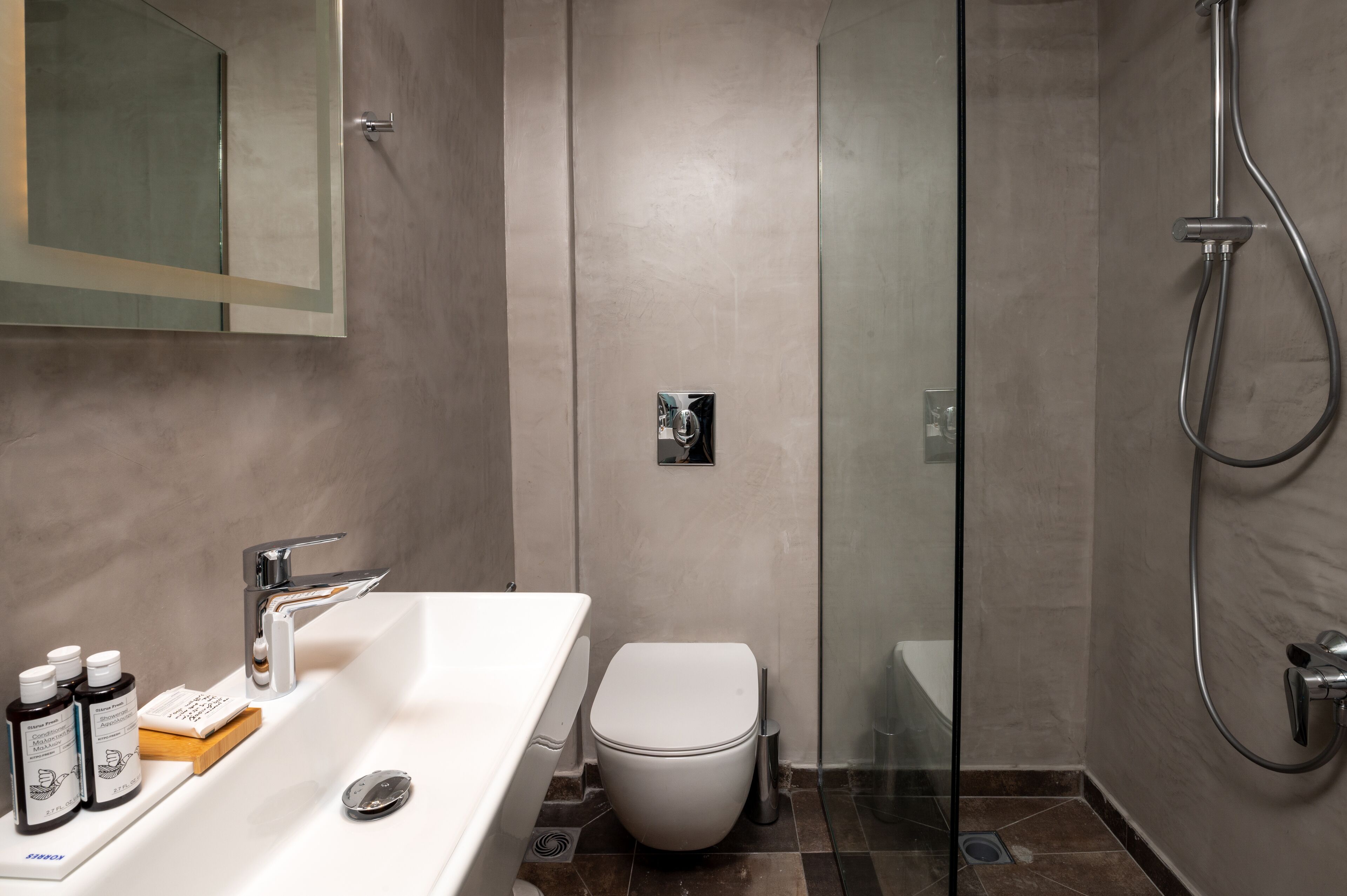 Un baño moderno con ducha envuelta en vidrio, un lavamanos blanco con artículos de aseo y un inodoro.