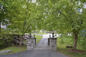 Un arc en pierre mène à un chemin pavé, entouré d’arbres verdoyants et d’un mur de pierres.