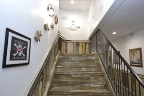 A wooden staircase with a metal railing, leading to a landing with a wall-mounted light fixture and a framed poster.