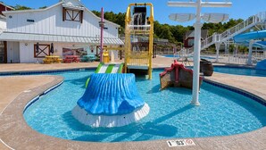 Una piscina con tobogán de agua, área de juegos y puesto de salvavidas.