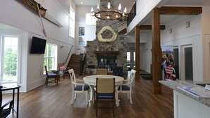 Una habitación amplia con techo alto, chimenea de piedra y zona de comedor con mesa y sillas redondas.