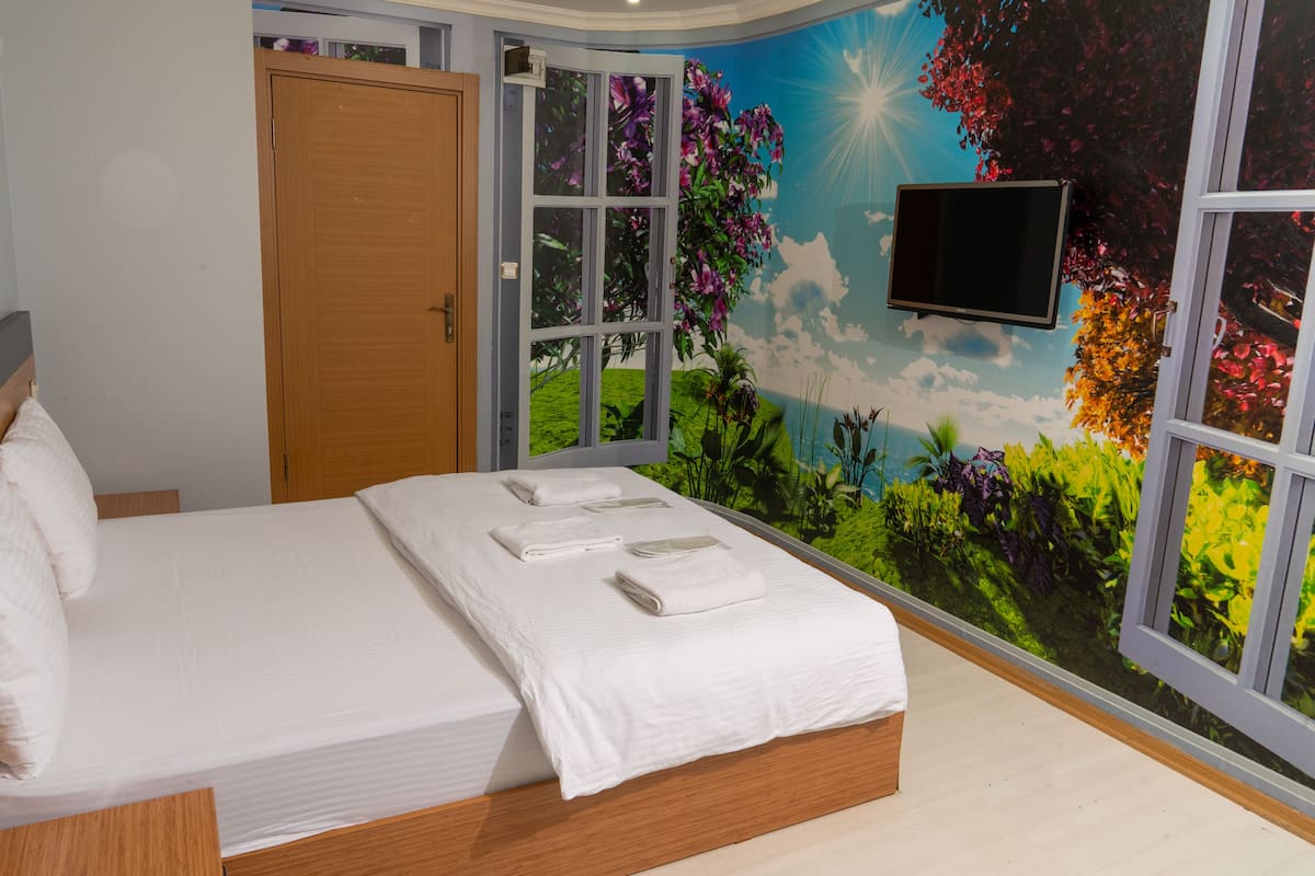 A bedroom with a bed, a TV on the wall, and a mural of a tropical scene.