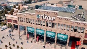 Un immeuble à plusieurs étages, reconnaissable à son grand panneau « TUYAP », doté de grandes fenêtres et d’une entrée centrale.