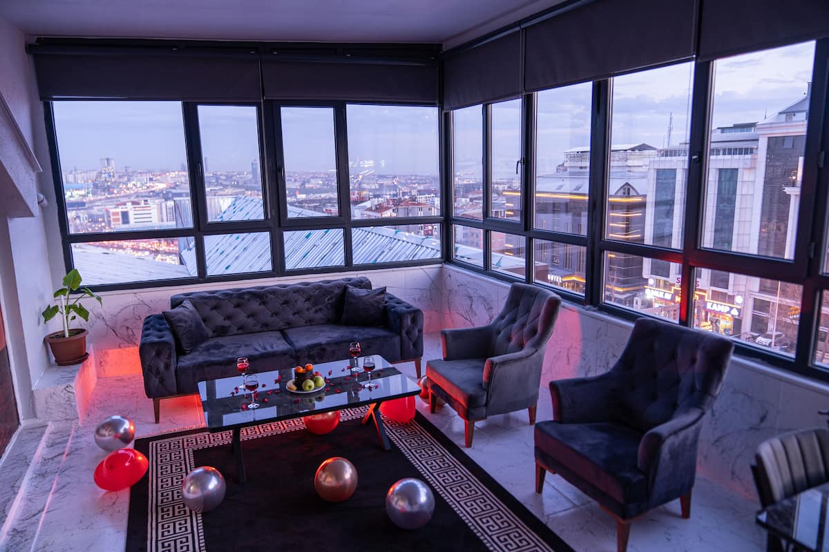 A modern living room with a large window, a black sofa, a glass coffee table, and a potted plant.