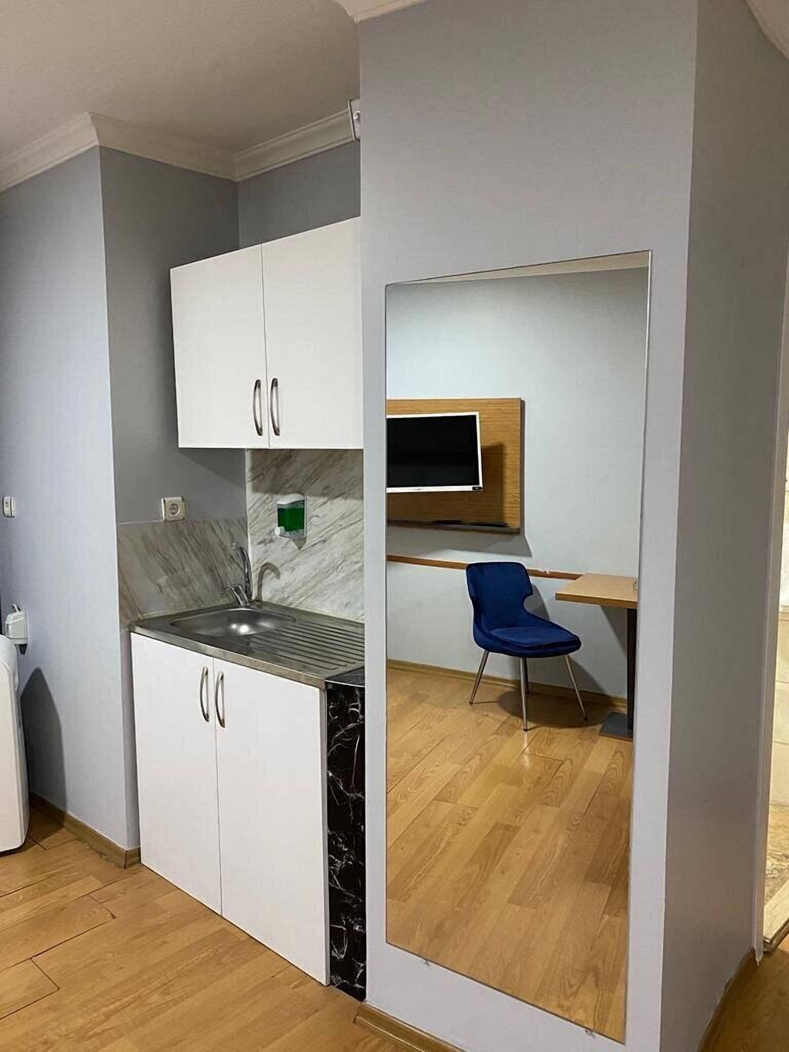 Una cocina compacta con armarios blancos, un lavamanos integrado y una mesa de comedor de madera con una silla azul.