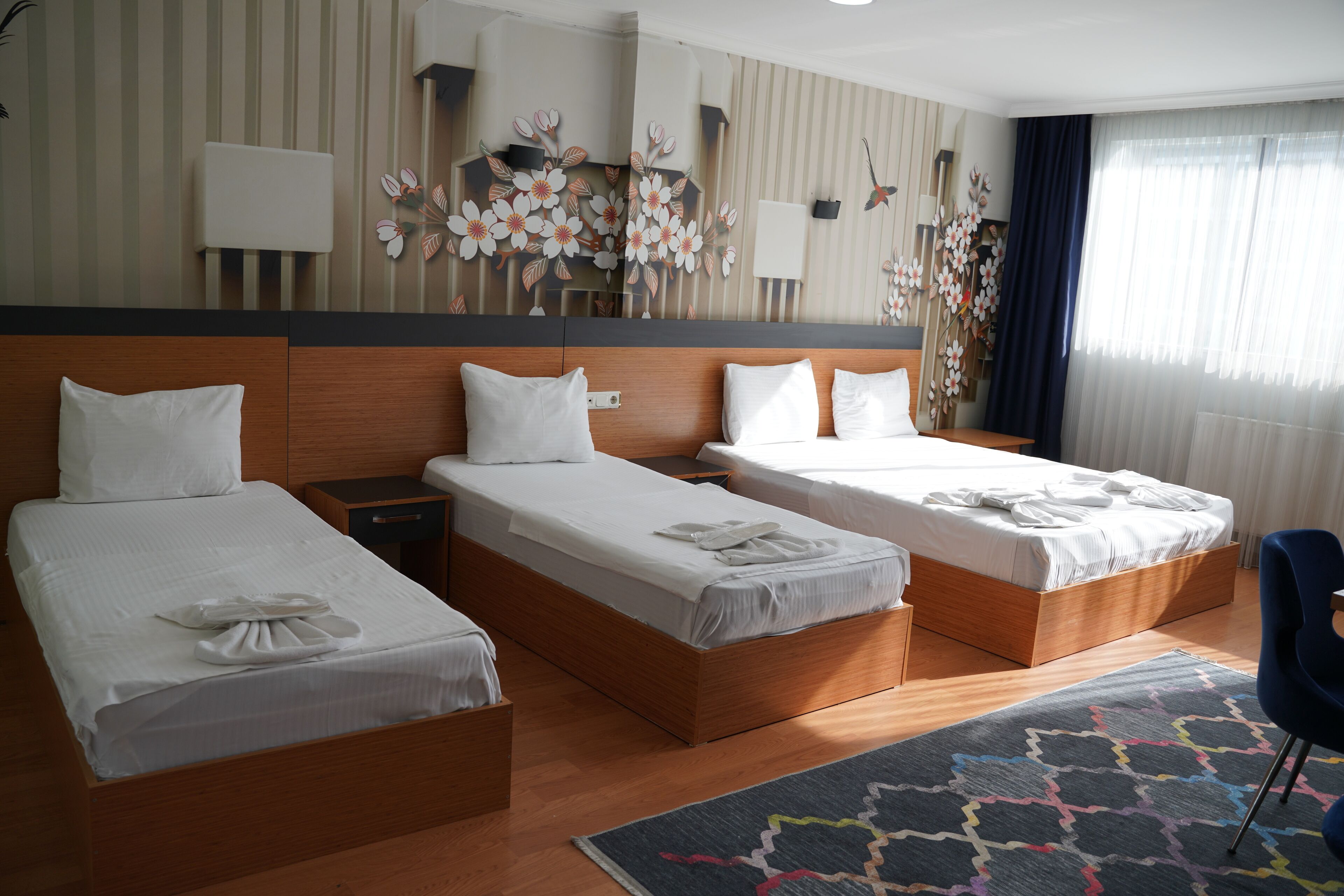 A hotel room with two single beds, a wooden headboard, a large mirror, and a floral wall decoration.