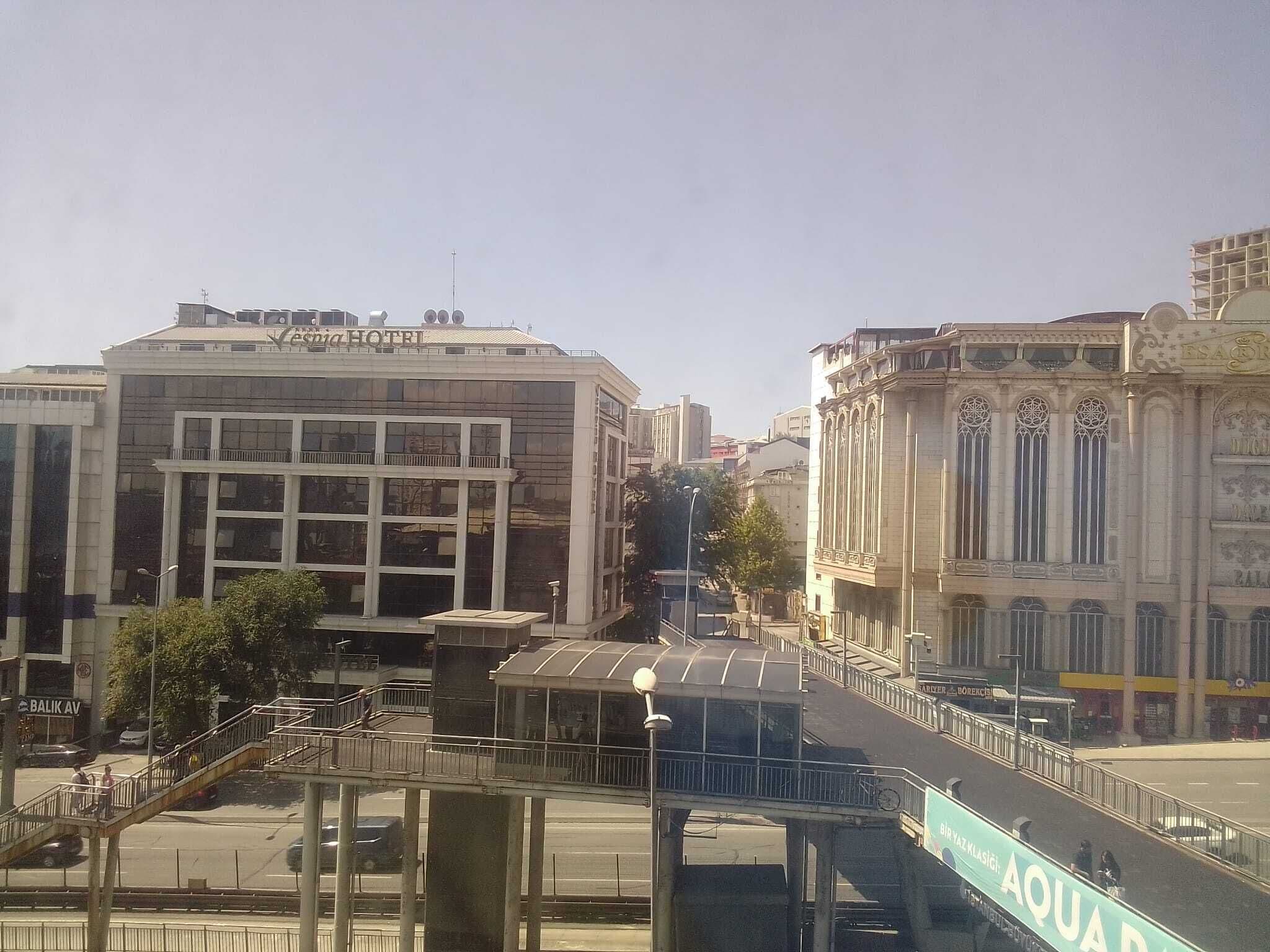 A hotel with a modern facade, a covered pedestrian walkway, and a street with a sign for 'AQUAD'.