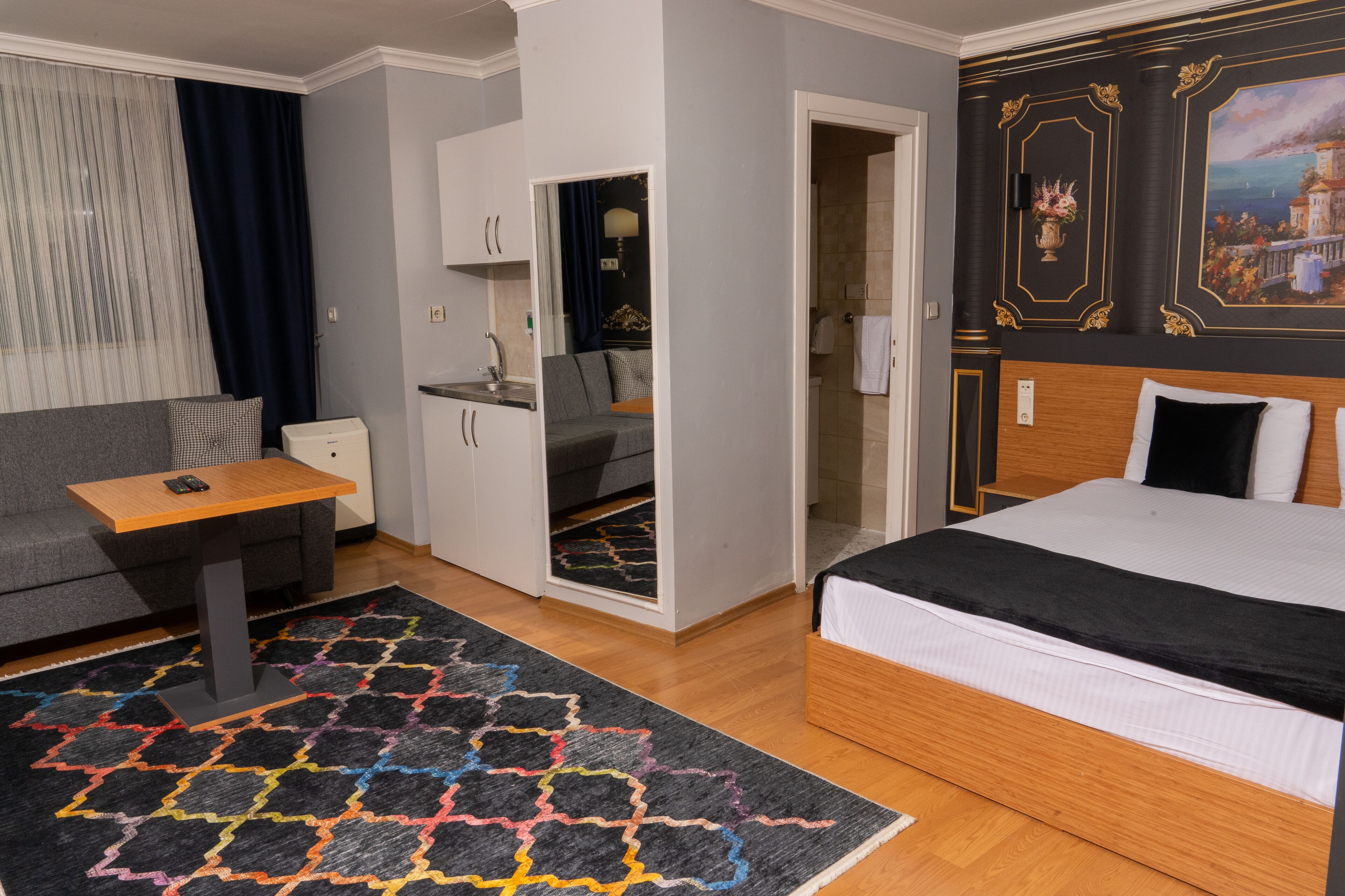 A hotel room with a bed, a sofa, a small table, a desk, and a bathroom visible through an open door.