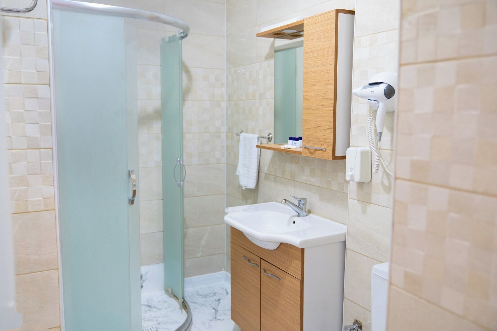 Une salle de bain avec une douche à parois de verre, un lavabo, un meuble en bois, un miroir et un sèche-cheveux.