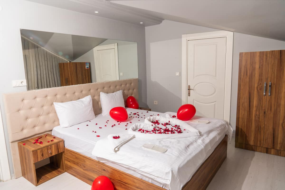 A bedroom with a large bed, a wooden nightstand, a mirror, a wardrobe, and red balloons.