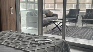 Una camera da letto con un letto grande, un armadio in legno e una porta a vetri scorrevoli che dà su un balcone con un divano e sedie.