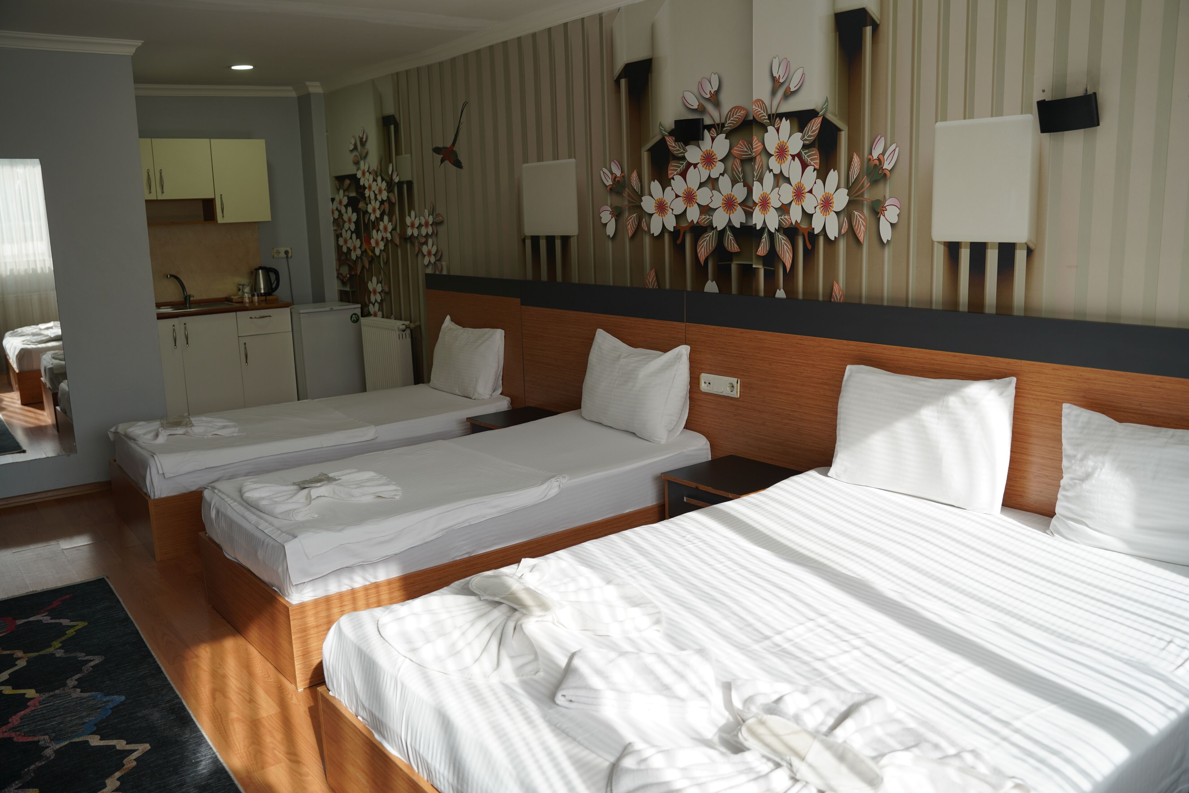 Een hotelkamer met drie eenpersoonsbedden, een klein kitchenette en een decoratieve wand met bloemmotieven.