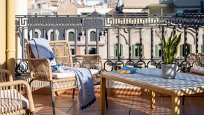 Un balcón con mobiliario de mimbre, una mesa y una planta en maceta.