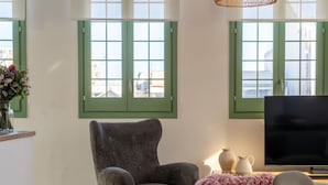 Una sala de estar con un sillón gris, un televisor de pantalla plana y un jarrón de flores sobre una mesa blanca.