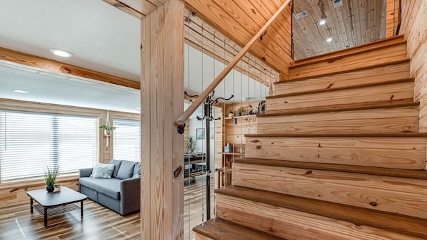 Una escalera de madera conduce a un altillo con un espacio habitable moderno, que incluye un sofá y una mesa de centro.