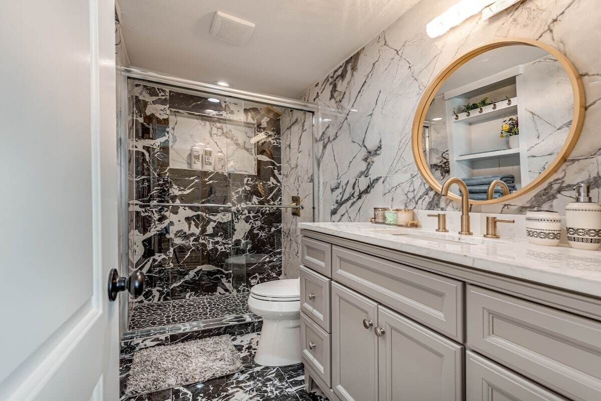 A bathroom with a marble vanity, a round mirror, and a toilet.