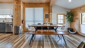 Una cocina moderna con electrodomésticos de acero inoxidable, una mesa de comedor de madera con sillas y un ventanal con persianas.